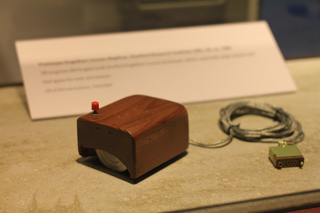 A wooden prototype computer mouse displayed with its cable.